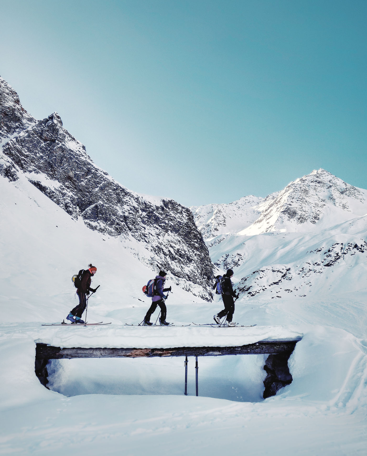 Eine Skitour im winterlichen Tirol, drei Skifahrer laufen über eine Brücke.